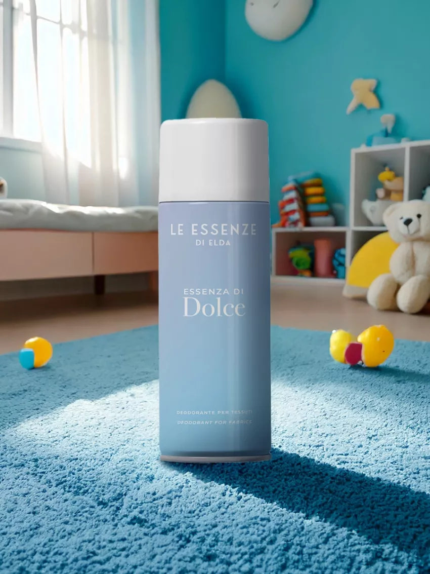 Dolce textílsprey 400ml frá Le Essenze di Elda í ljósbláum úðabrúsa með hvítu loki, á bláu teppi í barnaherbergi með leikföngum og bangsa.
