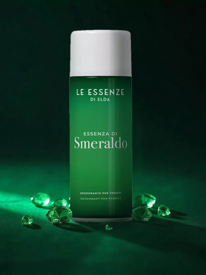 Smeraldo textílsprey 400ml frá Le Essenze di Elda í grænum úðabrúsa með hvítu loki, umkringt grænum skrautsteinum á dökkgrænum bakgrunni.
