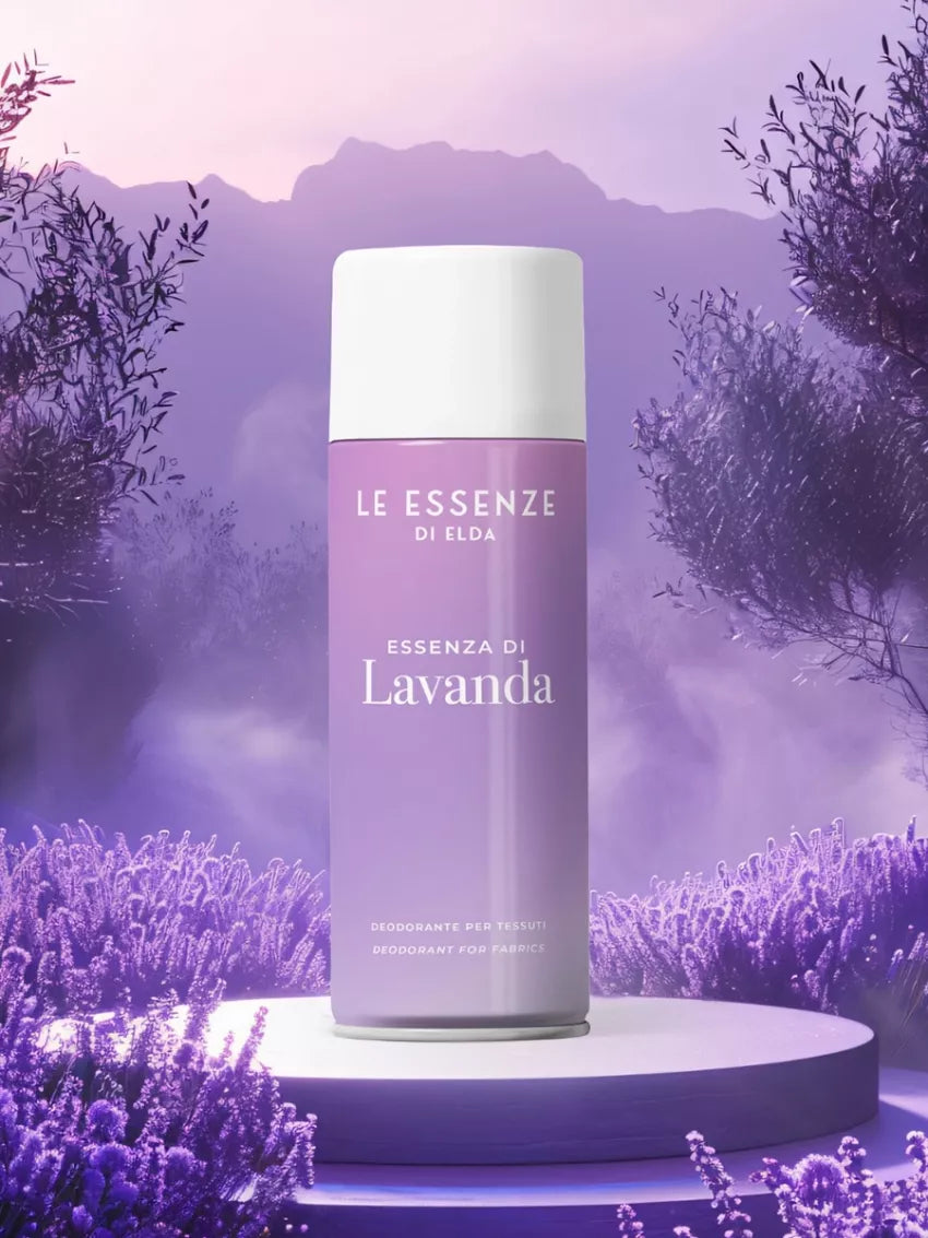 Lavanda textílsprey 400ml frá Le Essenze di Elda í ljósfjólubláum úðabrúsa með hvítu loki, á kringlóttum stalli meðal lavenderblóma með fjöll í bakgrunni.
